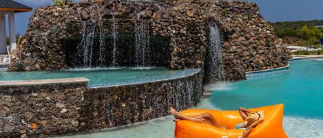 A pool with a waterfall feature and a person relaxing on an orange float.
