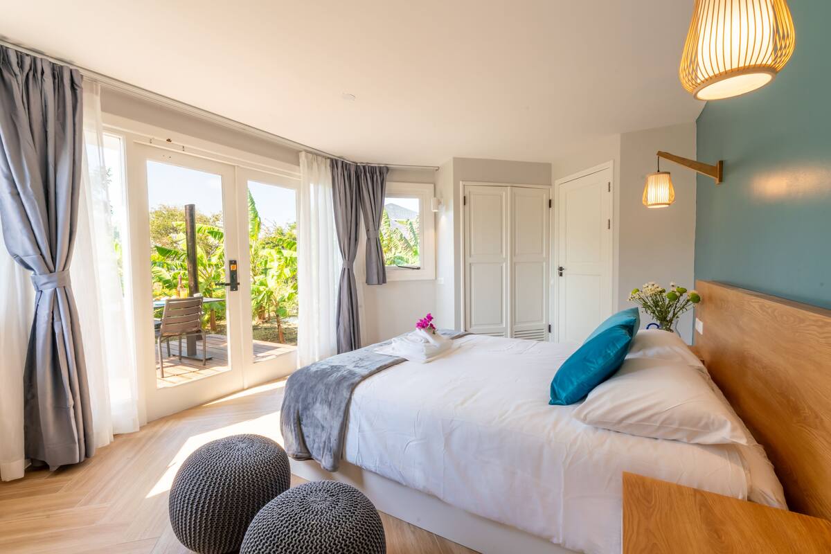 Un dormitorio con una cama grande, cabecera de madera y vistas a un patio con mesa y sillas.