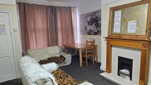 A living room with a sofa, a fireplace, a dining table, and a painting on the wall. - Beautiful 1-bed House in Leeds (Leeds)