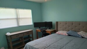 Ein Schlafzimmer mit einem Bett, einem Schreibtisch mit zwei Bildschirmen und einem Fenster mit Jalousien.