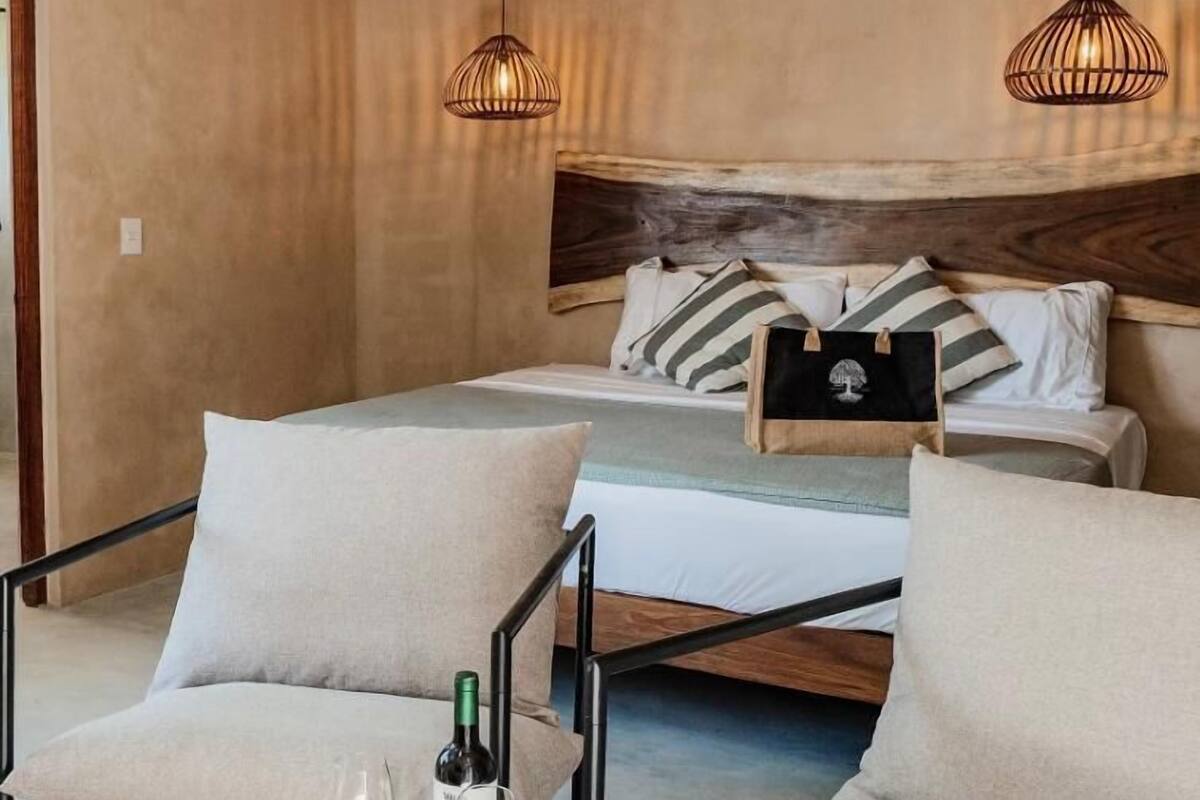 Een slaapkamer met een bed, twee stoelen, een tafel met een fles en glazen, en een airconditioner.