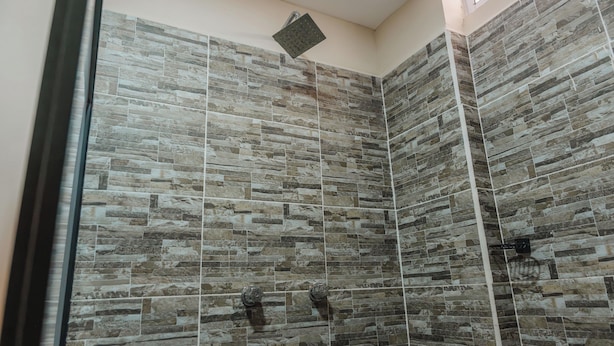 Une douche avec des carreaux de pierre et un pommeau de douche amovible.