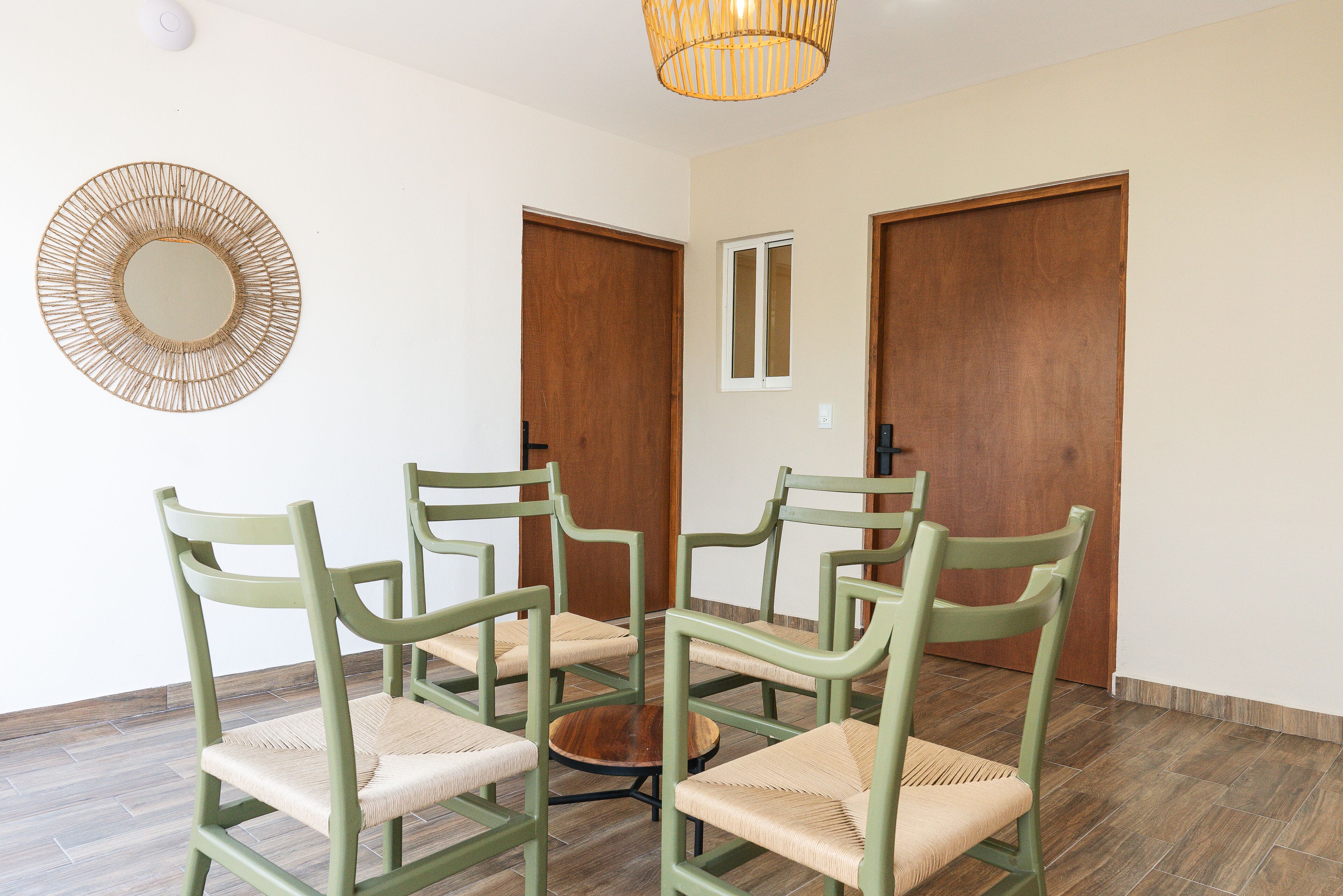 A room with four green chairs arranged around a small round table, wooden doors, and a wall-mounted mirror.