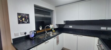 A modern kitchen with white cabinets, a black countertop, a window with blinds, a sink, and a cocktail menu on the wall.
