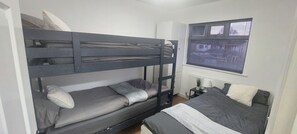 Et soveværelse med køjeseng, et vindue, et natbord med lampe og en radiator.