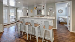 A kitchen with a bar area, wooden flooring, and a view to the bedroom. - Big Beautiful Beach House with private heated pool close to beach & everything! (Port Aransas)