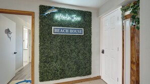 A hallway with a wall decorated with green foliage and a neon sign reading "Marlin Jane" and "BEACH HOUSE". - Big Beautiful Beach House with private heated pool close to beach & everything! (Port Aransas)