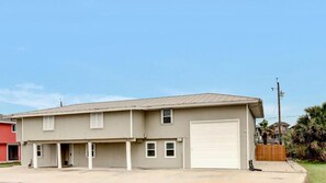 Un bâtiment à deux étages doté d’un garage, d’un espace de stationnement couvert et d’un petit jardin à l’avant.