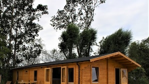 Una cabaña de madera con entrada de grava, ventanas amplias y un banco en el exterior.
