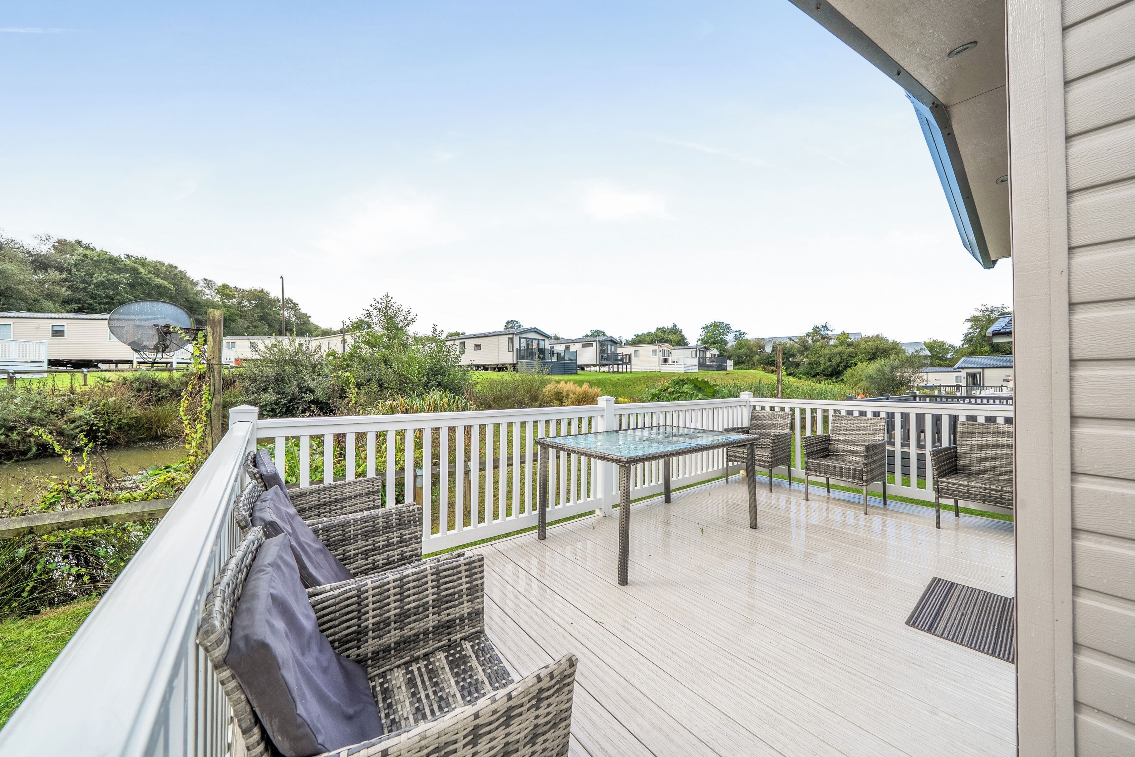 A deck with outdoor furniture, a glass-top table, and a view of mobile homes in the background.