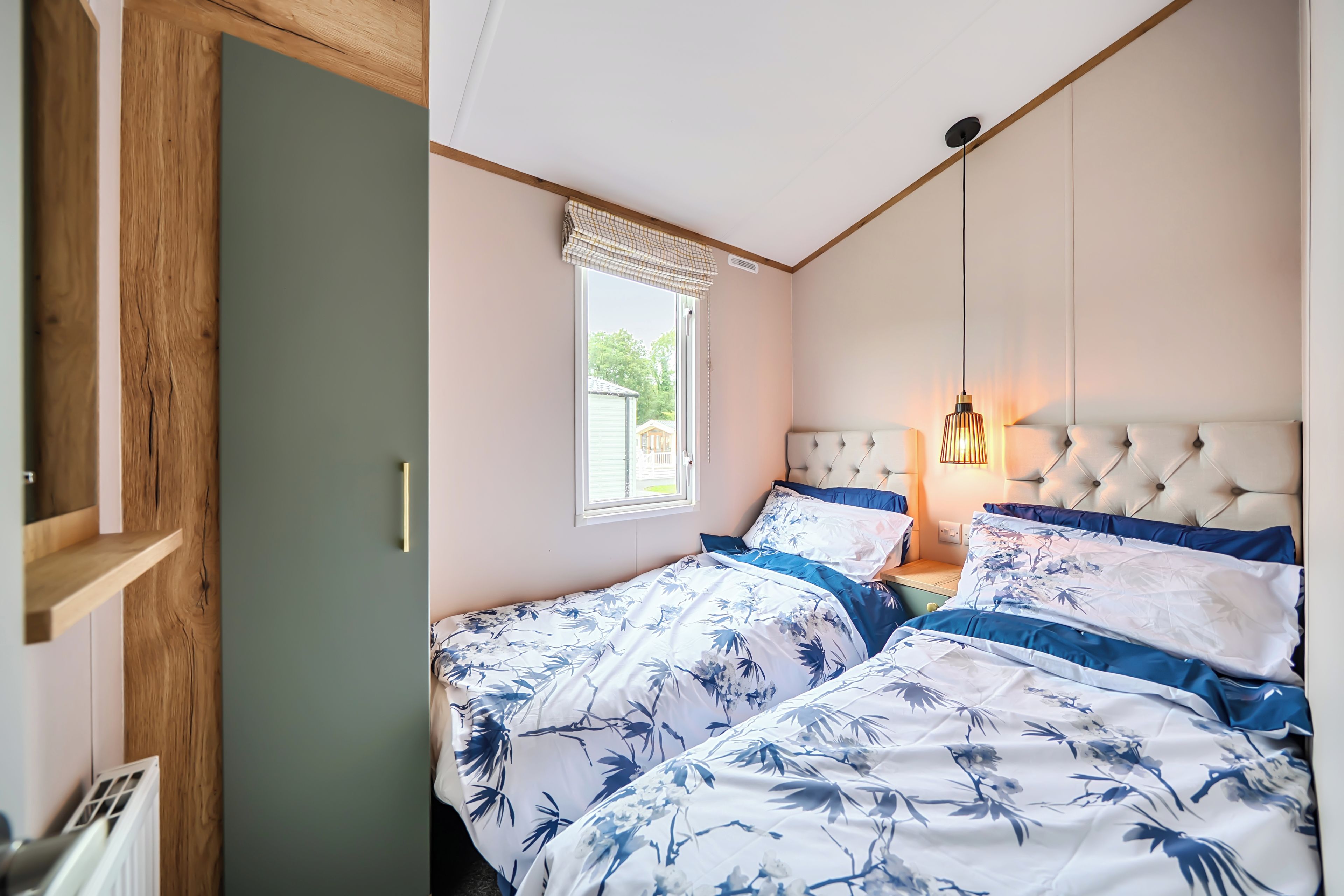 A bedroom with two beds, a window with blinds, a hanging light fixture, and a wooden door.