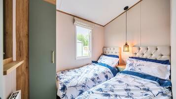 A bedroom with two beds, a window with blinds, a hanging light fixture, and a wooden door.