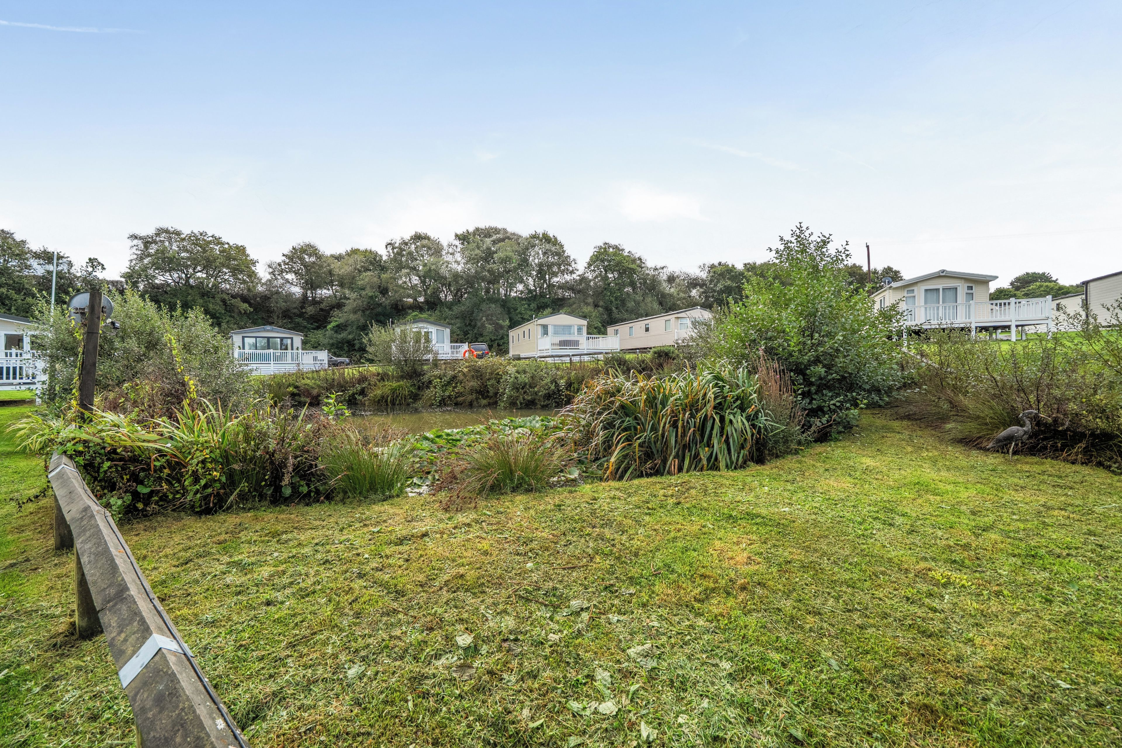 A grassy area with a wooden fence, a pond, and several mobile homes.