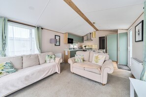 Un salon moderne avec un canapé, un petit divan et un coin cuisine à l’arrière-plan.