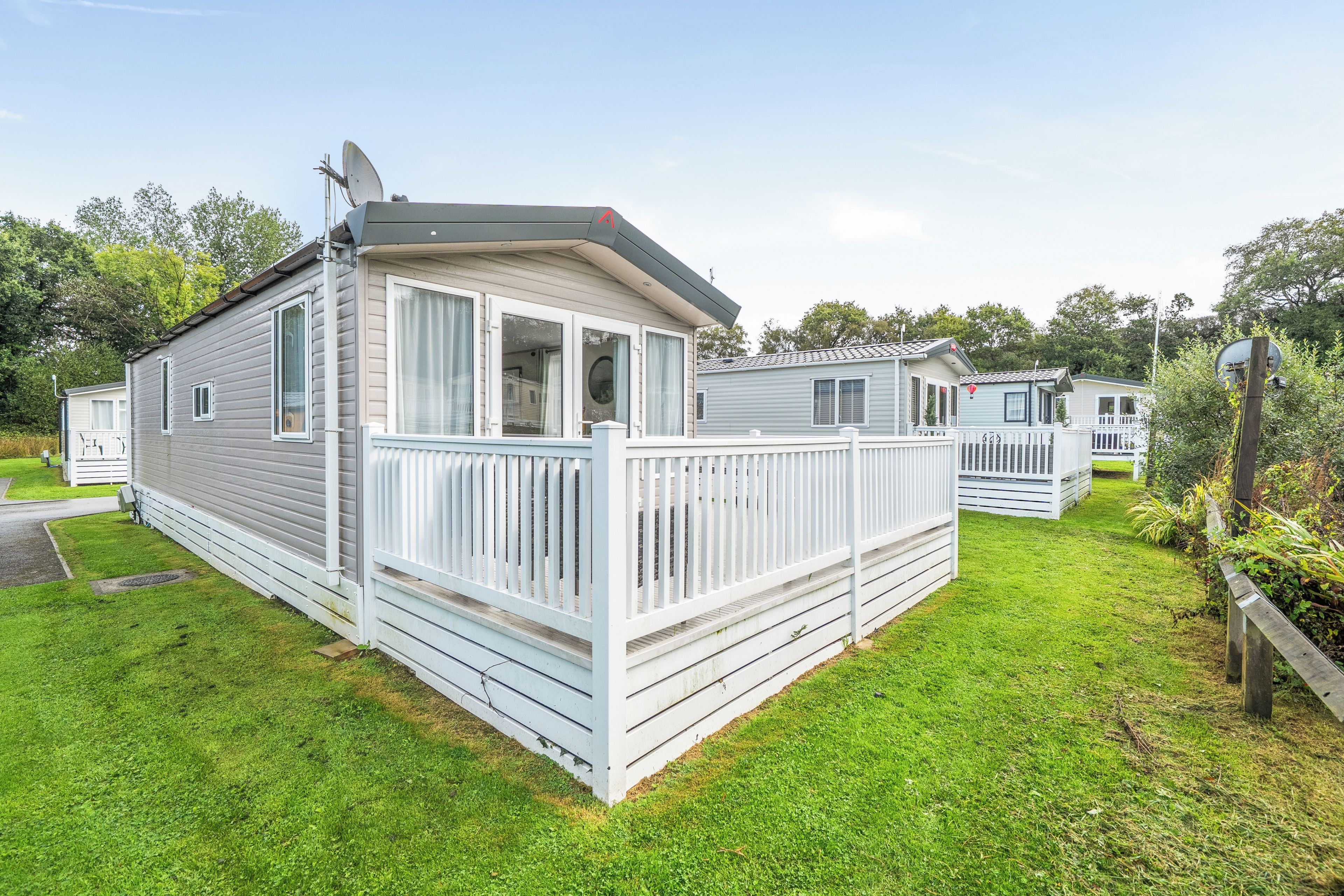 A mobile home with a fenced deck, satellite dish, and a grassy yard.