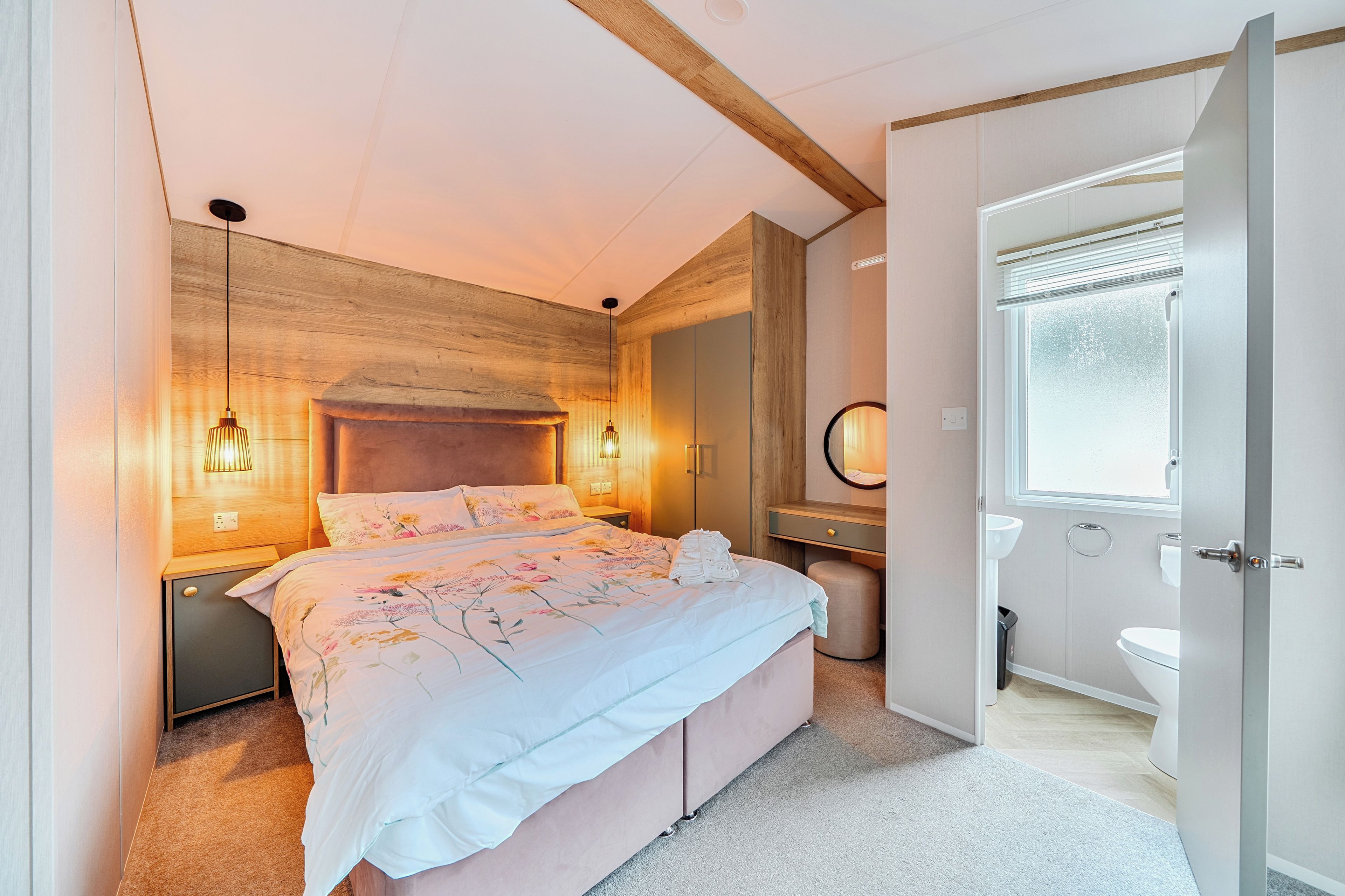 A bedroom with a bed, bedside tables, a nightstand, a mirror, and a view of the bathroom.