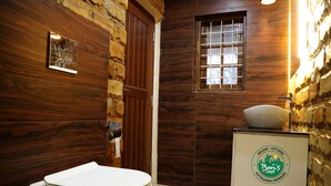 Un baño pequeño con pared de madera, inodoro blanco, ventana pequeña y lavamanos con un logotipo.