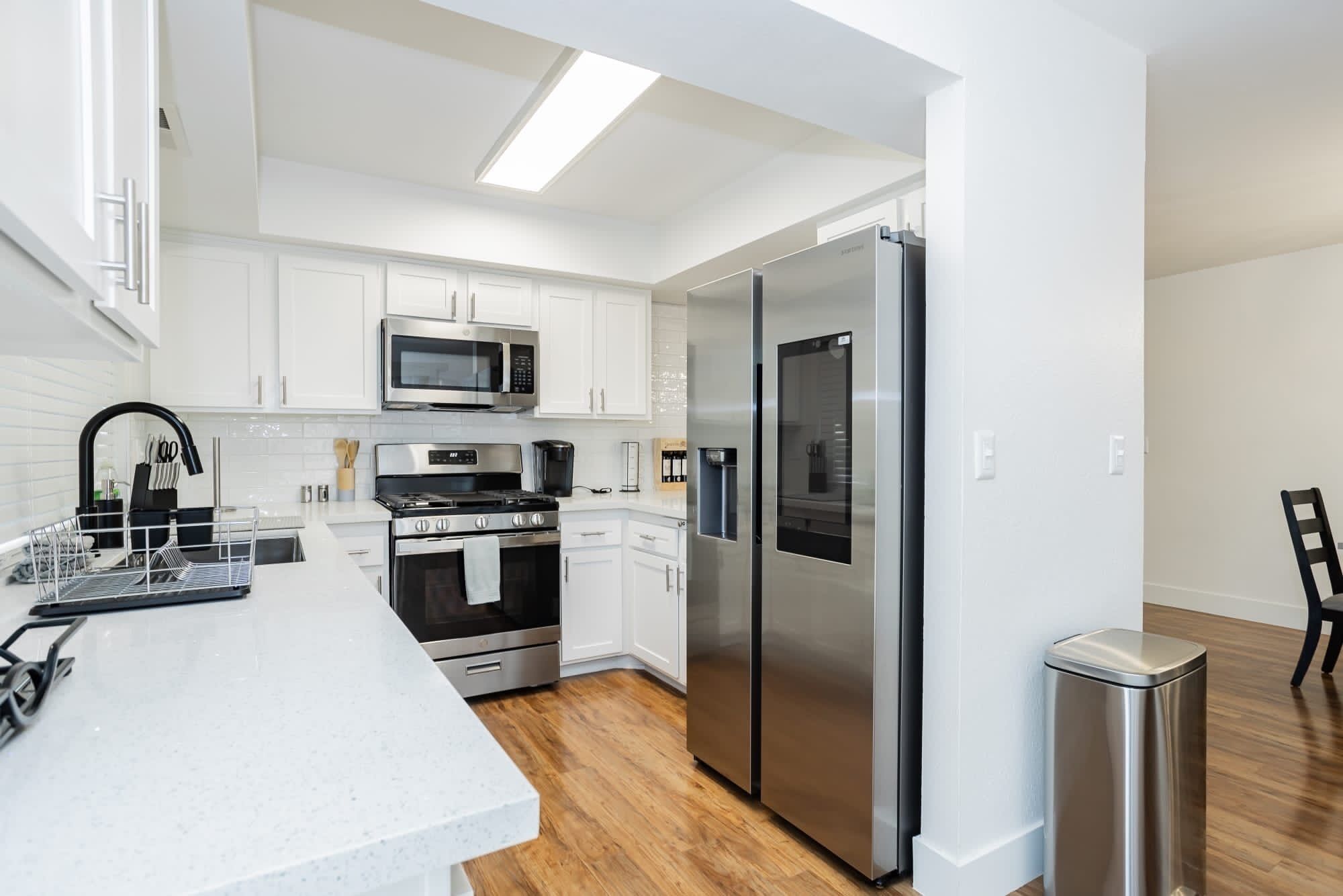 A modern kitchen with white cabinetry, stainless steel appliances, and a wooden floor.