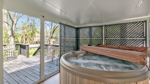 A hot tub on a wooden deck with a view of trees and a patio area.