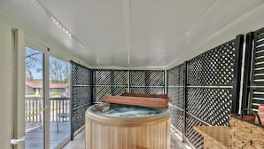 A hot tub with wooden seating and a table, surrounded by a black lattice fence.