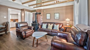A spacious living room with leather furniture, a fireplace, and exposed wooden beams.
