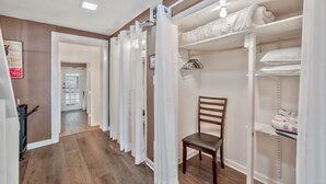 A hallway with wooden flooring, white curtains, a wooden chair, and a closet with shelves and hanging space.
