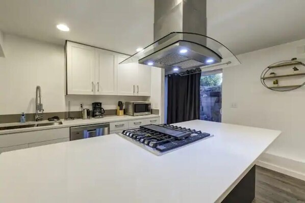 Une cuisine moderne avec des meubles blancs, un îlot central et un micro-ondes encastré.