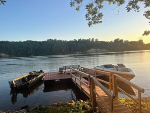 A wooden dock extending into calm water with a boat docked on the left and a motorboat on the right. - Waterfront Barndominium with Pool Table & Dock (Tucker)