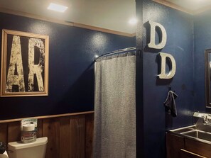 A bathroom with a dark blue wall, a wooden vanity, a toilet, and a shower curtain. - Waterfront Barndominium with Pool Table & Dock (Tucker)