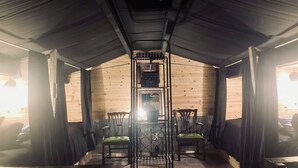 Ein gemütlicher, schwach beleuchteter Raum mit Holzwänden und einer geneigten Decke. Zwei Stühle mit grünen Kissen und ein Metallgestell stehen in der Mitte.