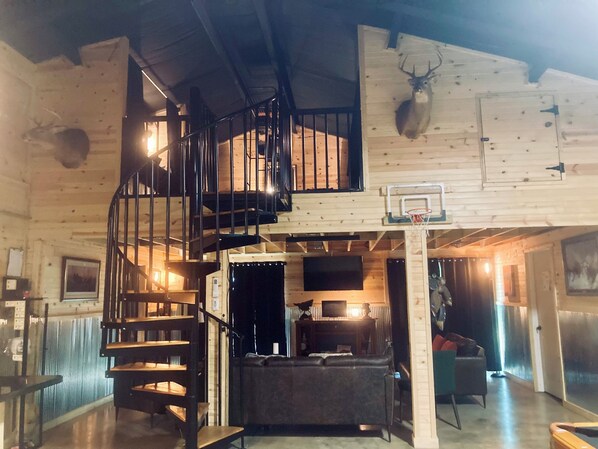 A spacious interior with a spiral staircase, a basketball hoop, and a cozy seating area. - Waterfront Barndominium with Pool Table & Dock (Tucker)