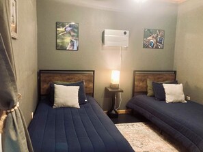 A room with two beds, a nightstand with a lamp, and two wall-mounted air conditioners. - Waterfront Barndominium with Pool Table & Dock (Tucker)