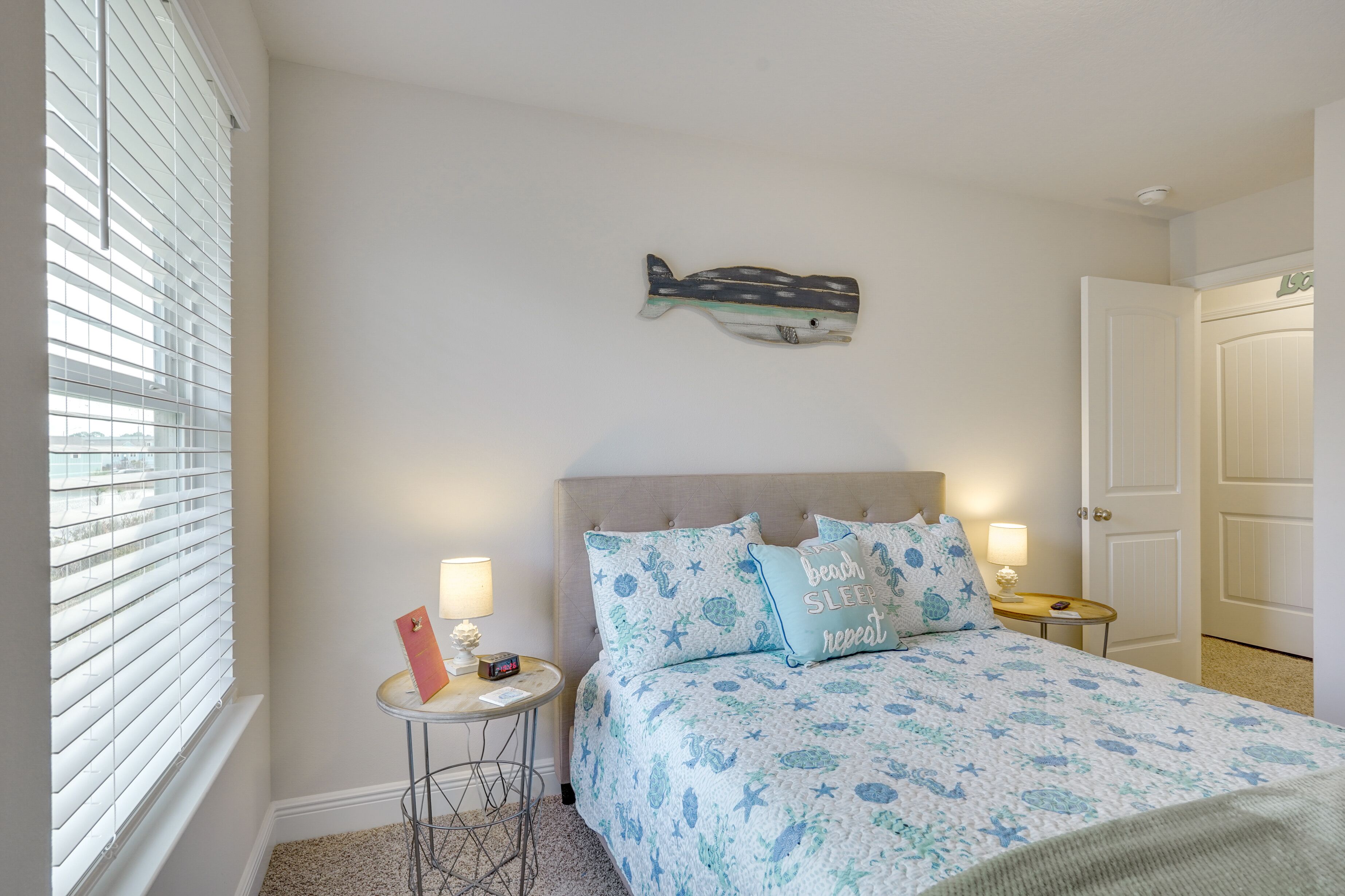 A bedroom with a bed, a nightstand, a wall-mounted fish decoration, and a window with blinds.