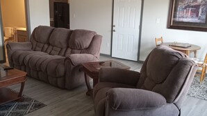 A living room with a sofa, a recliner, a coffee table, and a dining table. - Beautiful retreat with gameroom and outdoor grill. (Myrtle Beach)