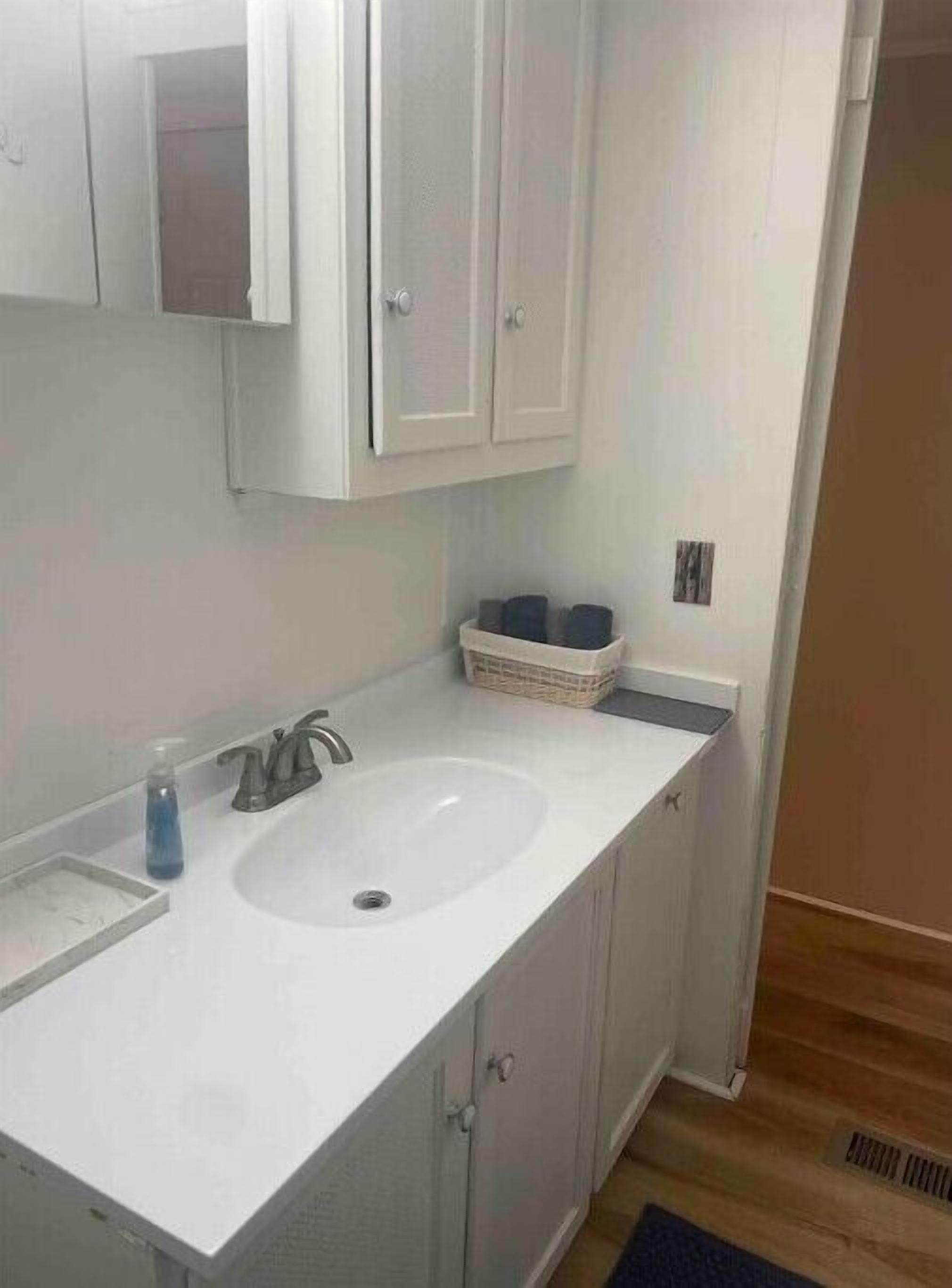 Un baño con un lavamanos blanco, un espejo y un mueble sobre el lavamanos.