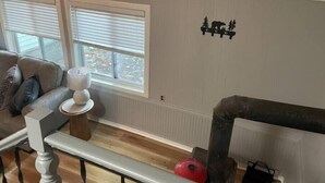 Olohuoneessa on sohva, lamppuvarrella varustettu pöytä, patteri ja seinätarra, jossa on kuvattuna puita.