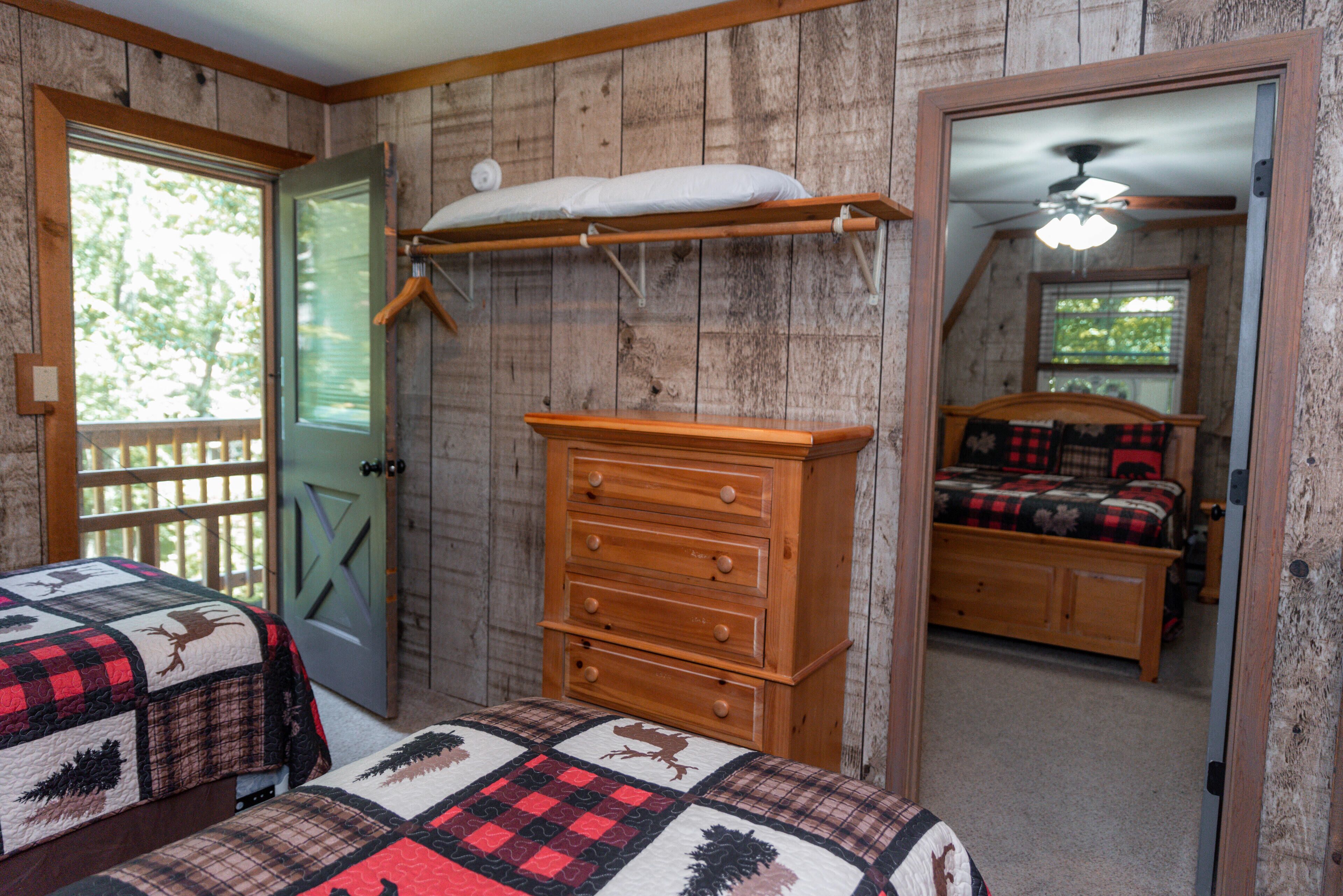 A bedroom with a wooden dresser, a bed with a quilt, a window with a view of trees, and a door.