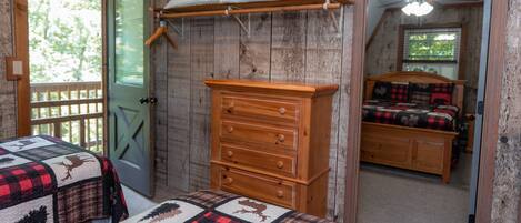A bedroom with a wooden dresser, a bed with a quilt, a window with a view of trees, and a door.