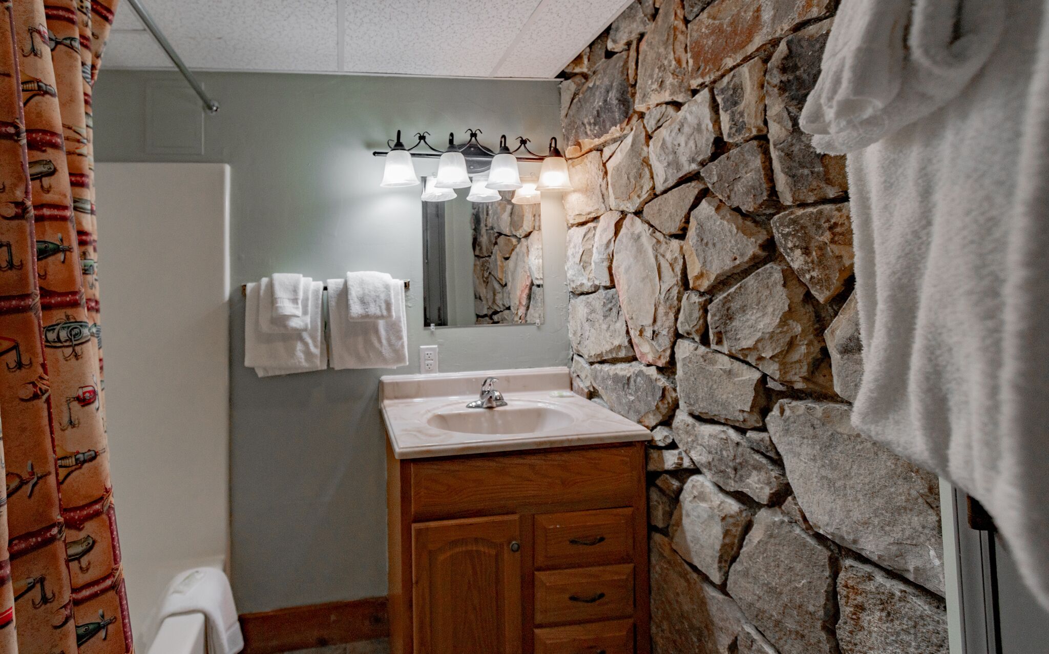 Un baño con pared de piedra, un mueble de madera, un lavabo y un espejo con iluminación.