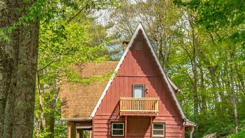 Un chalet rustique doté d’un balcon, entouré d’une végétation luxuriante et agrémenté d’une terrasse en bois.