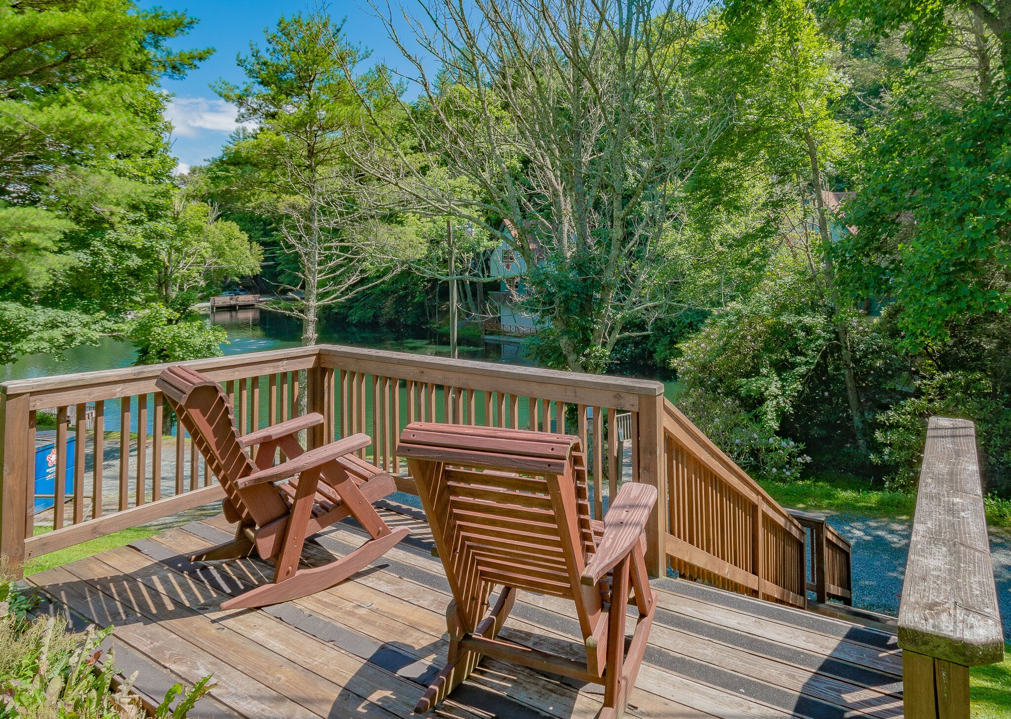 A wooden deck with two rocking chairs and a view of a lake surrounded by trees.