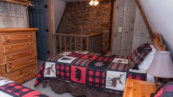 A bedroom with a wooden dresser, a bed with a quilt featuring animal prints, a stone wall, and a wooden staircase.