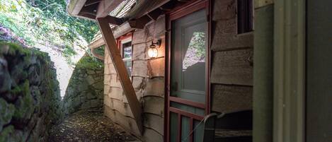 A wooden cabin with a stone wall, a wooden deck, and a window with a view of trees.