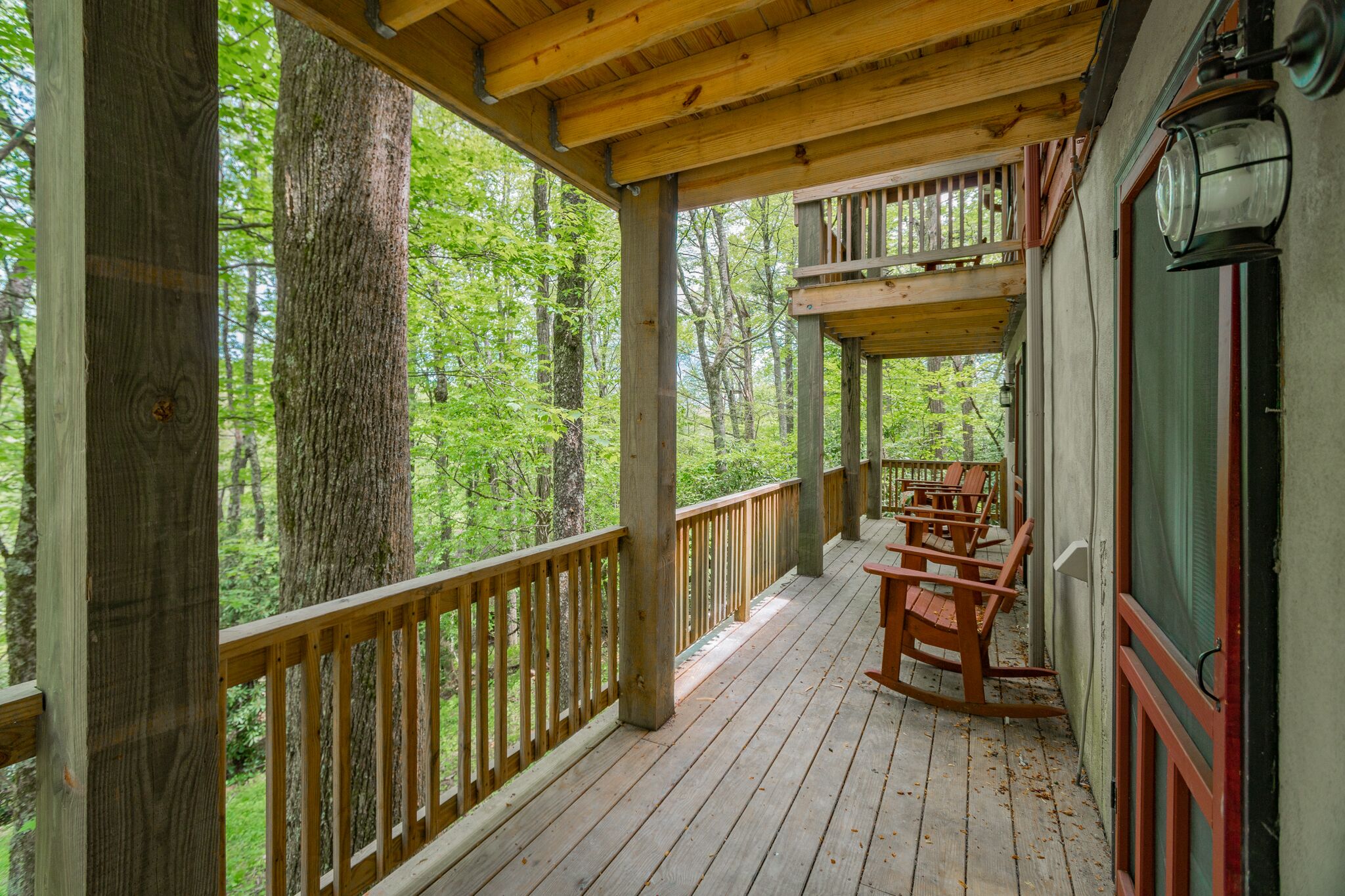Une terrasse en bois avec une rambarde, entourée d’arbres, et un espace avec des bancs.