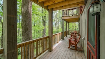 Une terrasse en bois avec une rambarde, entourée d’arbres, et un espace avec des bancs.