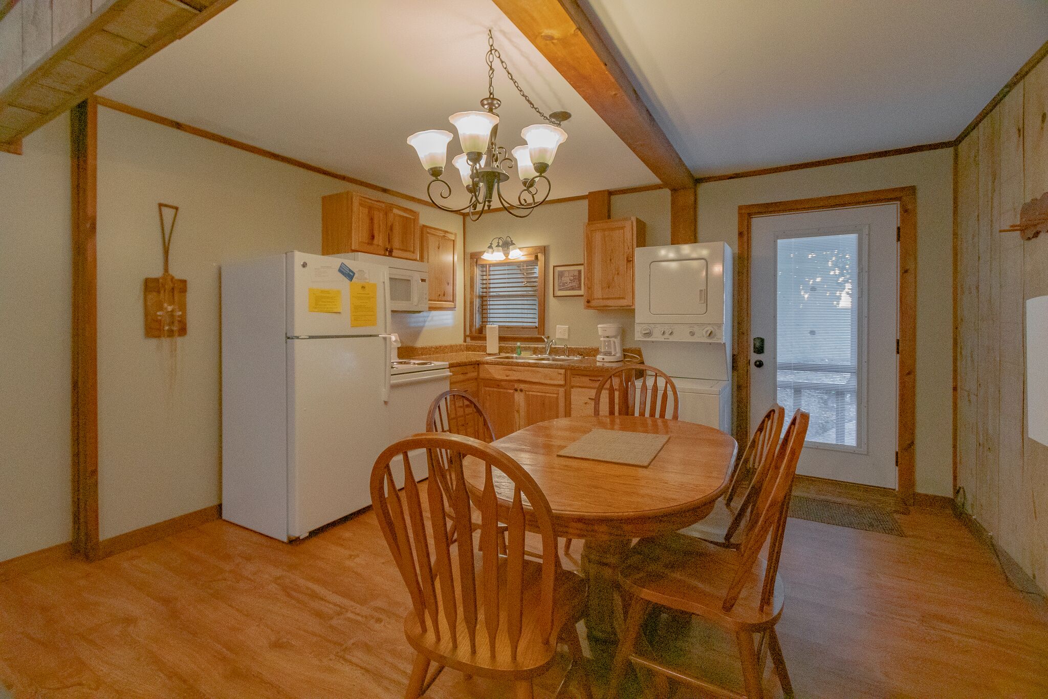 A kitchen with wooden cabinets, a dining table with chairs, a refrigerator, a microwave, and a chandelier.