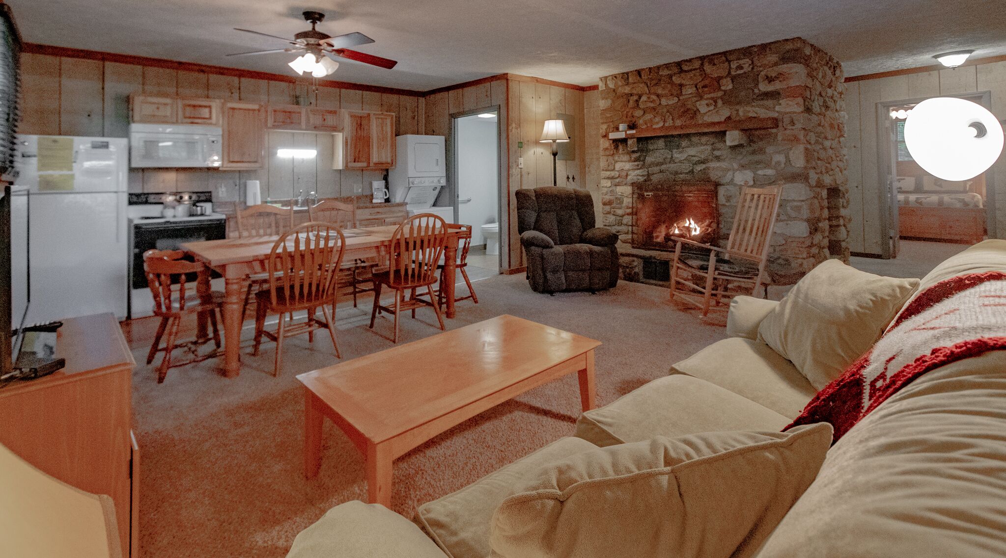 Un salon chaleureux avec une cheminée, un coin repas avec des meubles en bois et une cuisine aux murs en pierre.