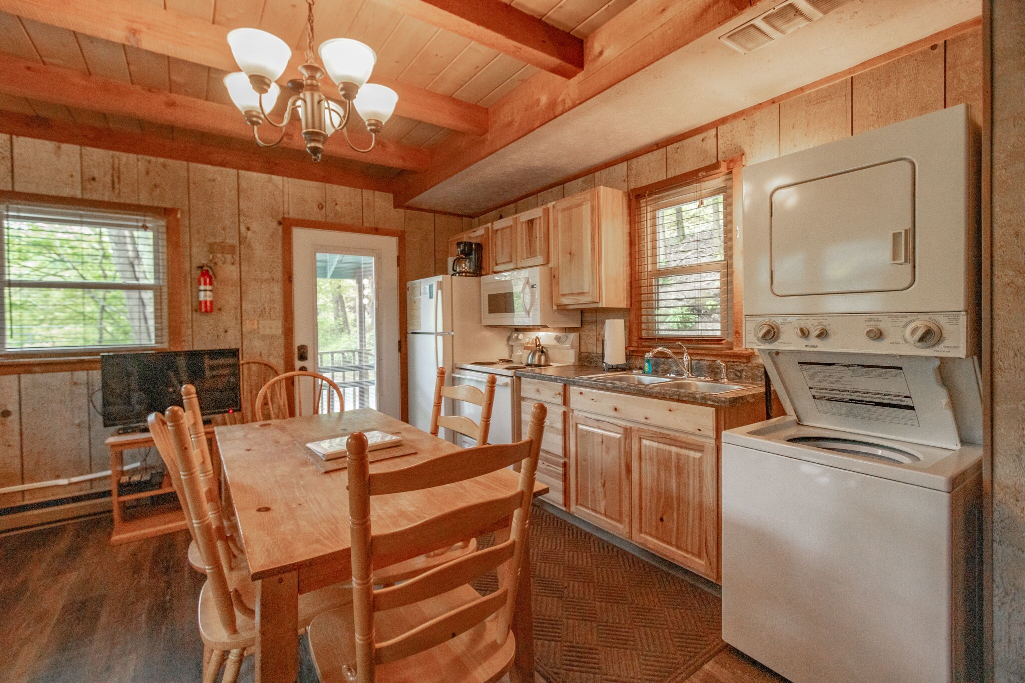 Cocina de cabaña de madera con una mesa de comedor, sillas, un refrigerador, un microondas, una estufa y un televisor.