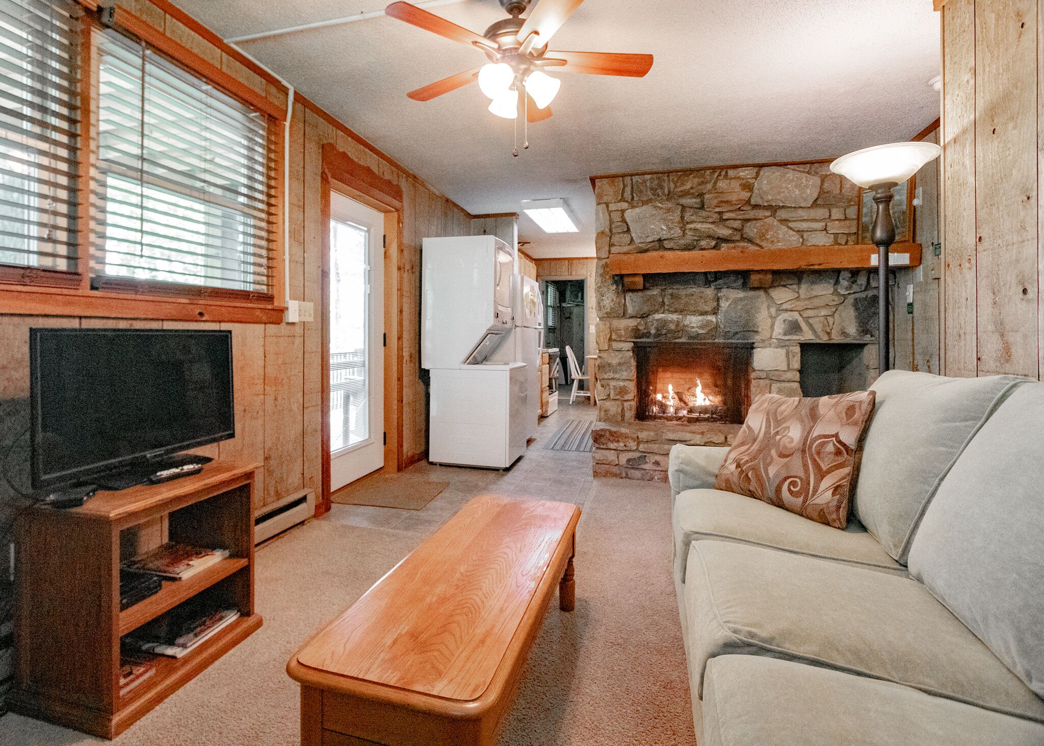 A cozy living room with a stone fireplace, a television, and a wooden bench.