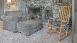 A cozy living room with a stone fireplace, a wooden staircase, a gray sofa, and a rocking chair. - Swiss Mountain Village (Blowing Rock)